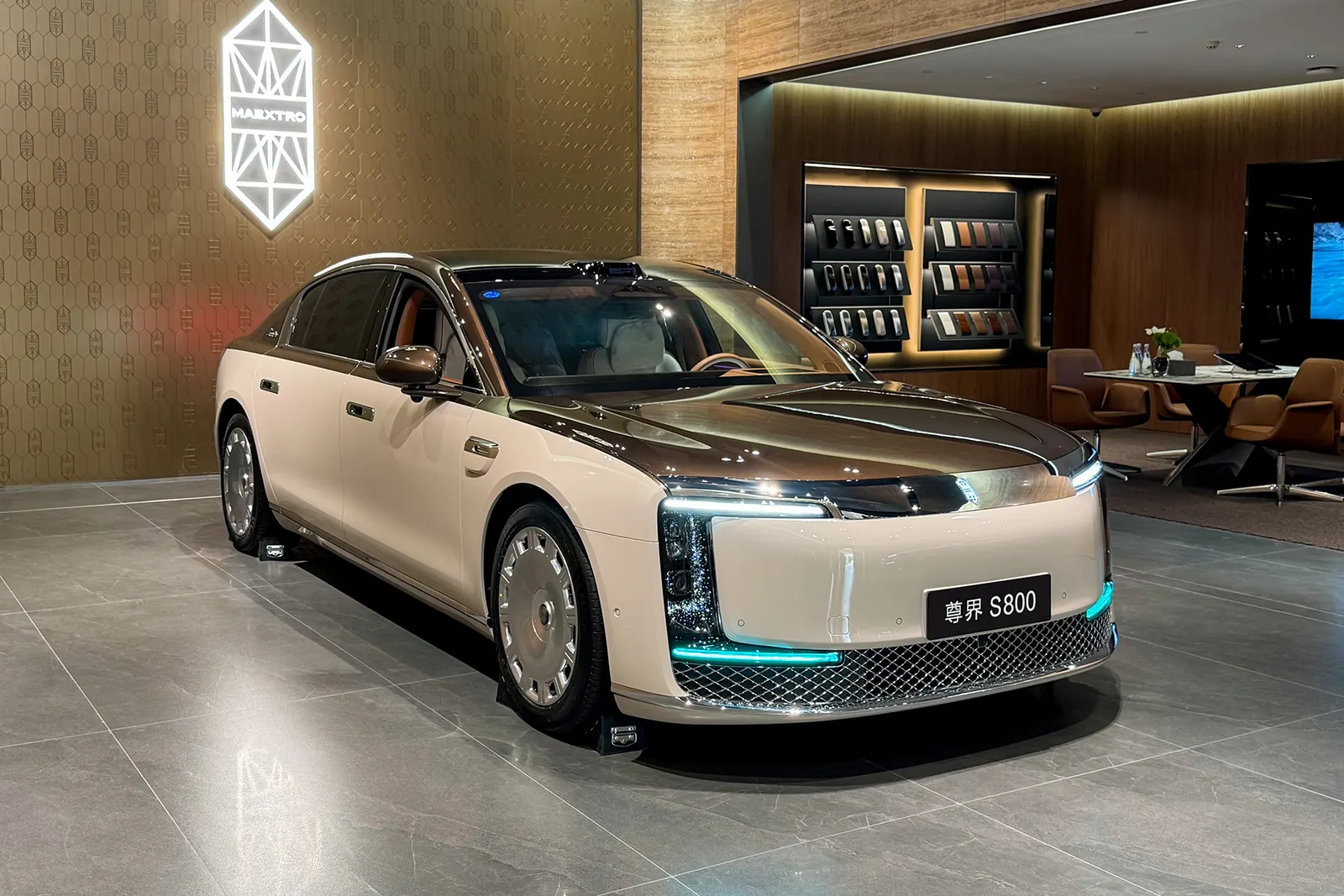 سيارة Maextro S800 بلون الشمبانيا والبني في صالة عرض وعلى الجدار شعار Maextro