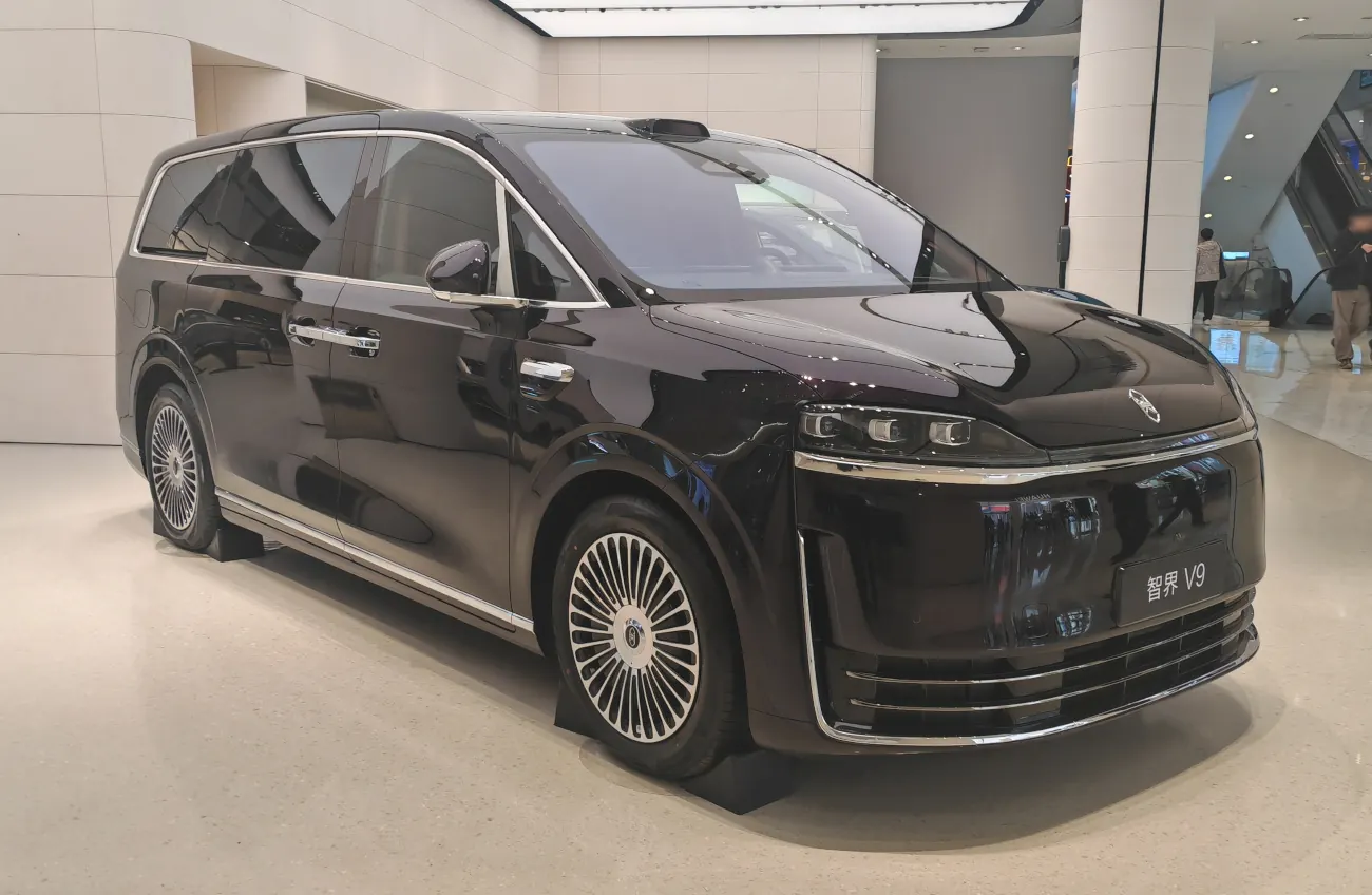 منظر ثلاثي الأرباع من الأمام لسيارة Luxeed V9 داكنة في صالة عرض داخل مجمع تجاري